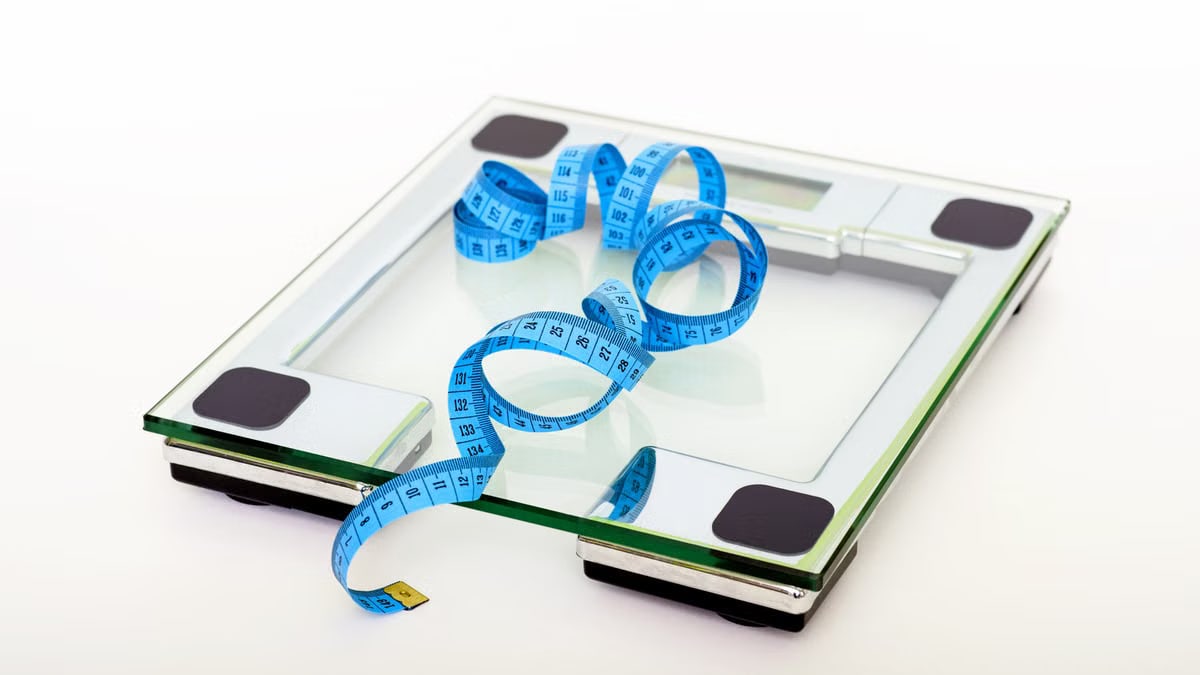 A digital glass weighing scale with a blue measuring tape, symbolizing weight management.